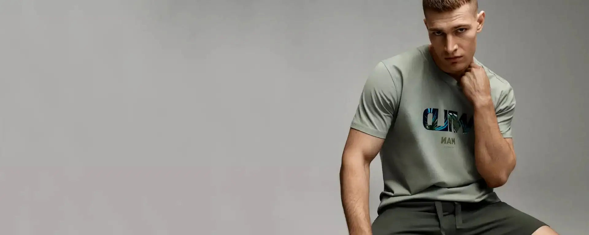 Un uomo che indossa una t-shirt a maniche corte grigio chiaro con la parola 'climb' stampata sul petto in lettere grasse blu scuro.